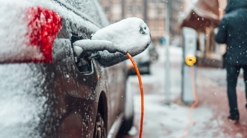 Ηλεκτρικό αυτοκίνητο που φορτίζει στο χιόνι. Πορτοκαλί καλώδιο ηλεκτρικής φόρτισης. Ηλεκτρικά αυτοκίνητα τον χειμώνα
